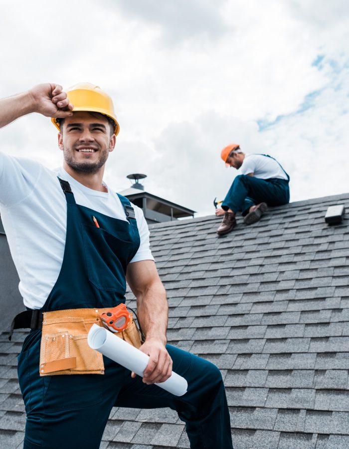 selective-focus-of-happy-repairman-holding-rolled-paper-while-coworker-repairing-roof.jpg